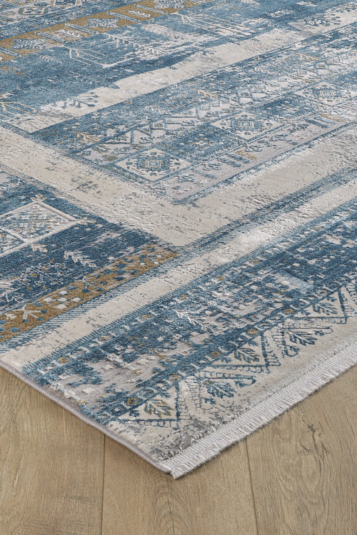 Load image 1 in gallery view. A close-up of the Cool Nomadica Premium Rug - M366B, a machine-made rug with blue, beige, and gold tones in geometric and floral patterns, fringed edges, and a subtle distressed finish on a light wood floor.