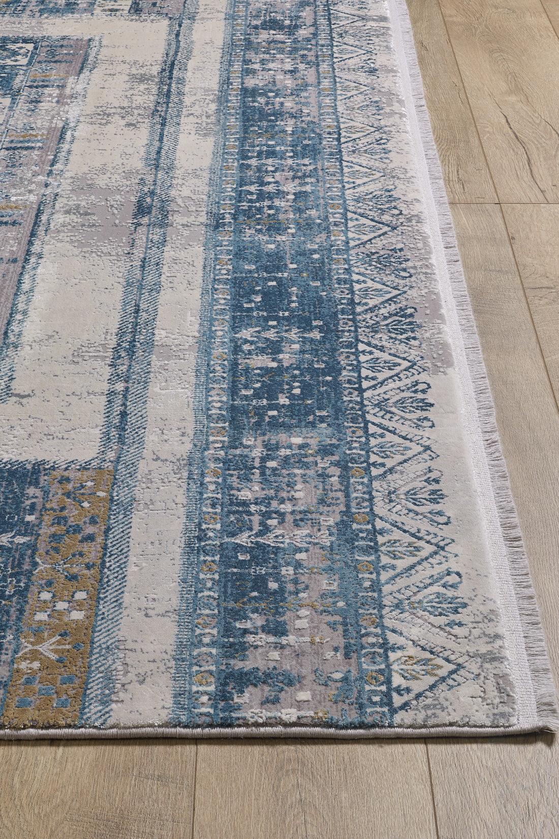 A close-up of the Cool Nomadica Premium Rug - M366B, a machine-made piece in blue, beige, and gold with geometric and detailed border patterns, displayed on a light wooden floor.