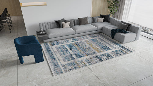Load image 1 in gallery view. Modern living room with a large gray sectional, dark pillows, blue armchair, and the Cool Nomadica Premium Rug - M366B on light marble tile flooring. Floor-to-ceiling windows fill the space with natural light.