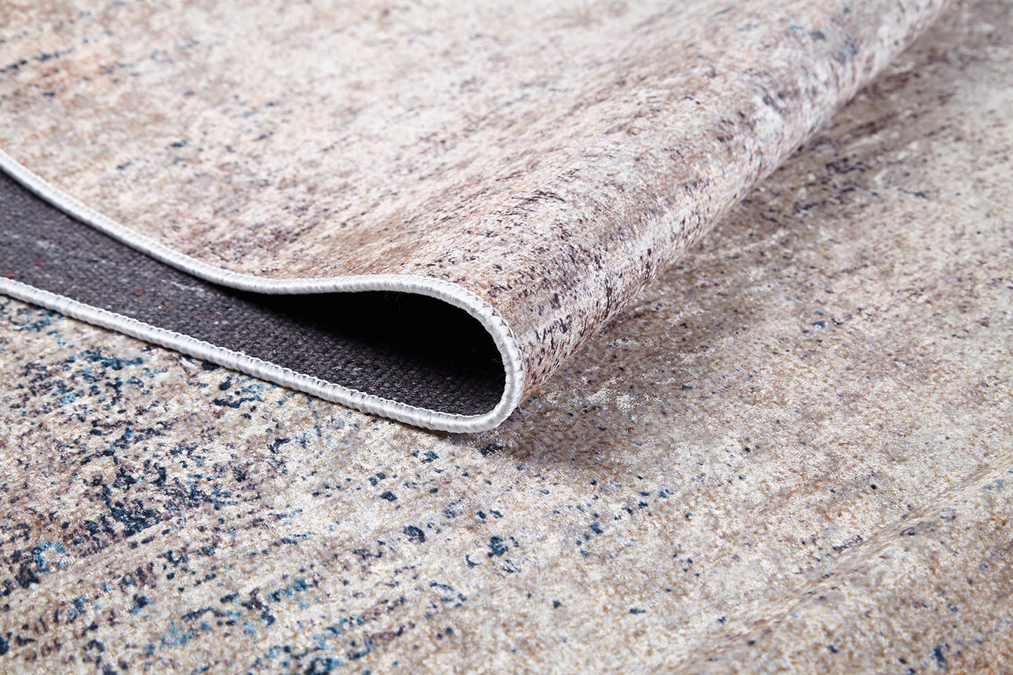 A close-up of the Copper Glow - Washable Rug - JR1700 (Custom Size) in beige and grey, with a lifted corner showing its dark underside, stitched edge, textured surface, and sturdy build—perfect for high-traffic areas.