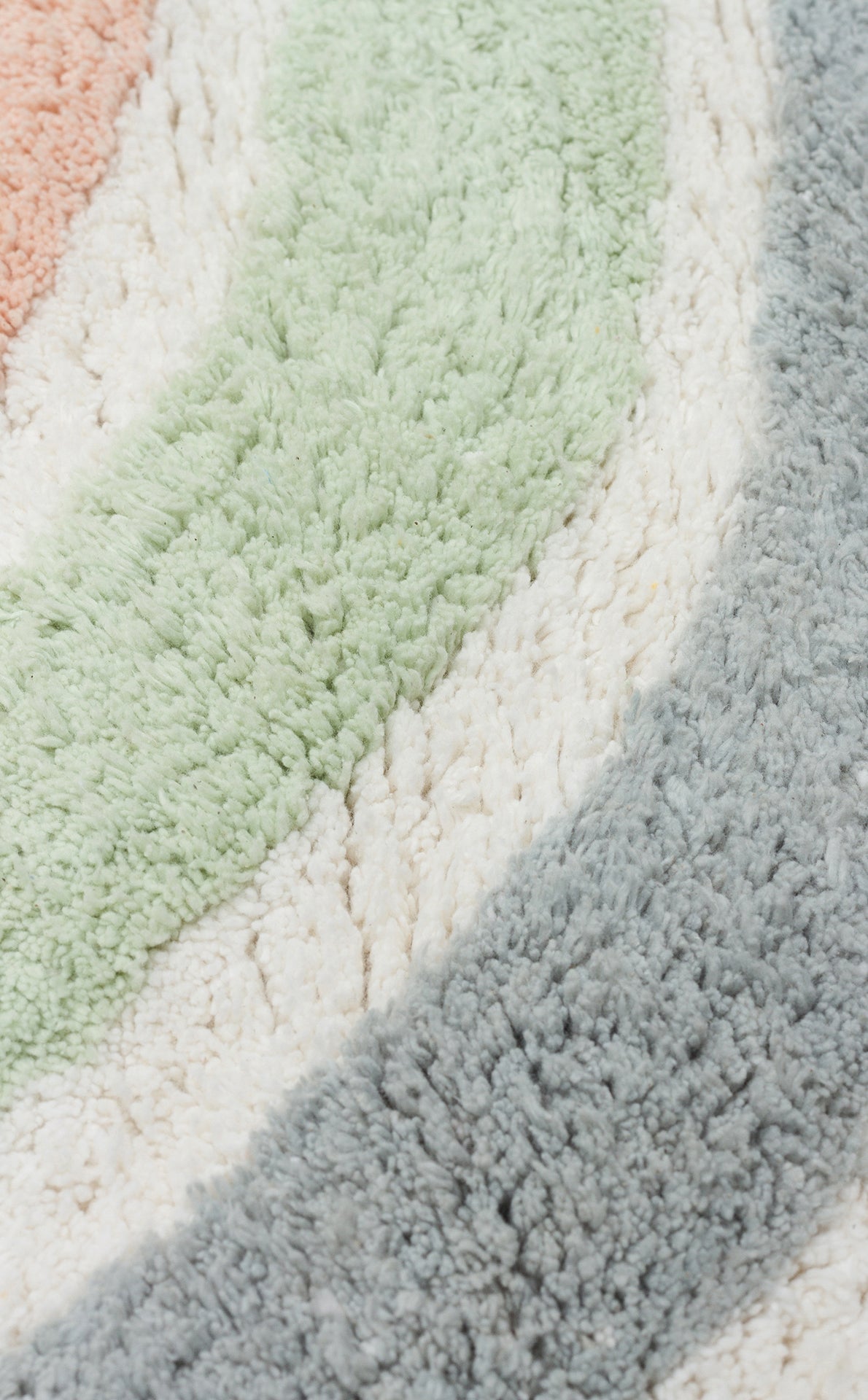 Close-up of the Cozy Puzzle - Washable Shaggy - CBN07 kids’ room rug, featuring wavy stripes in pastel peach, mint green, off-white, and light gray. This plush, washable rug has a soft texture for a cozy and inviting feel.
