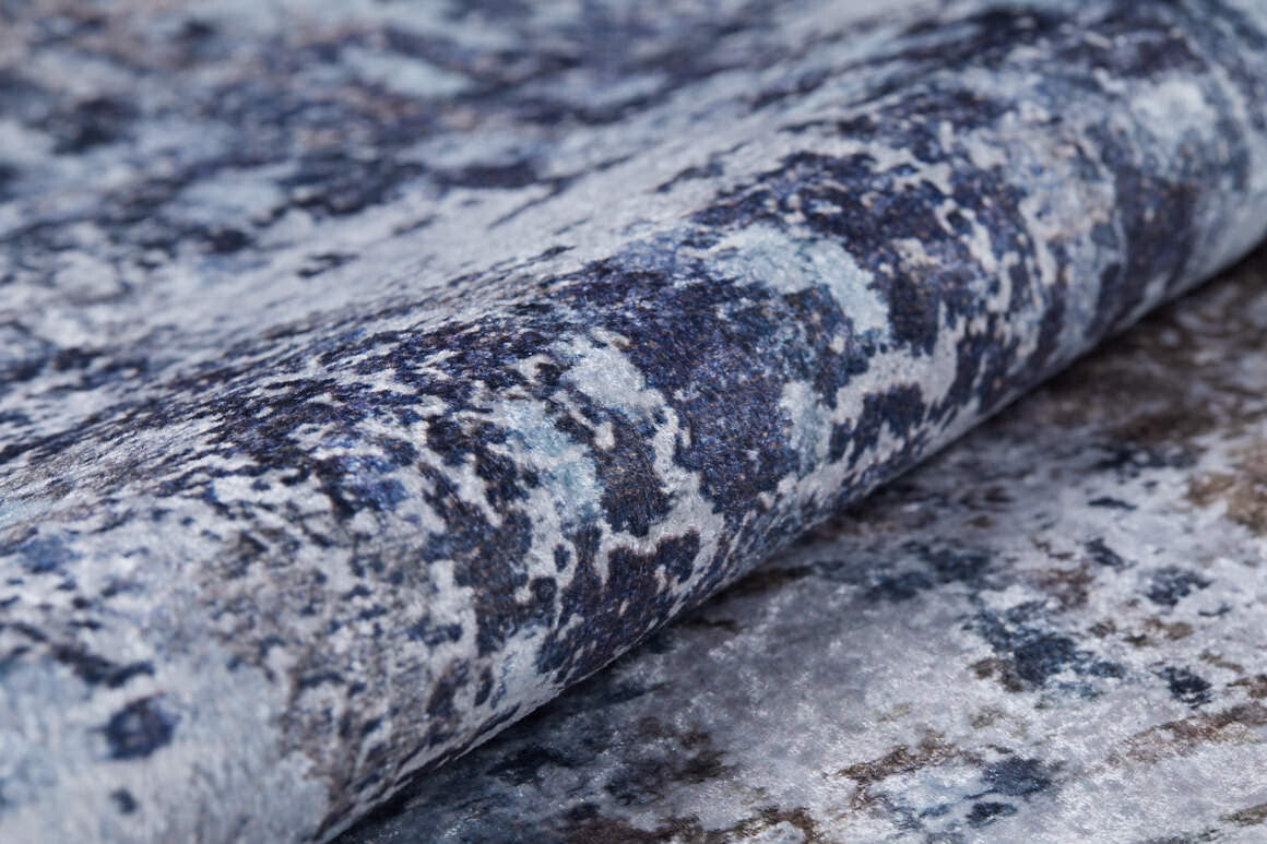 Close-up of the Creative Currents - Washable Rug - JR835 (Custom Size), showcasing its abstract marbled pattern in blue, gray, and white, partially rolled to display its plush thickness and detailed surface.