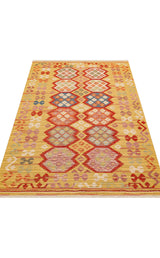 The Crimson Dot - Kilim - NMD03 is a polyester flat weave rug with a yellow background, featuring rows of red, blue, pink, and green geometric diamond patterns in an ethnic kilim style and a textured appearance.