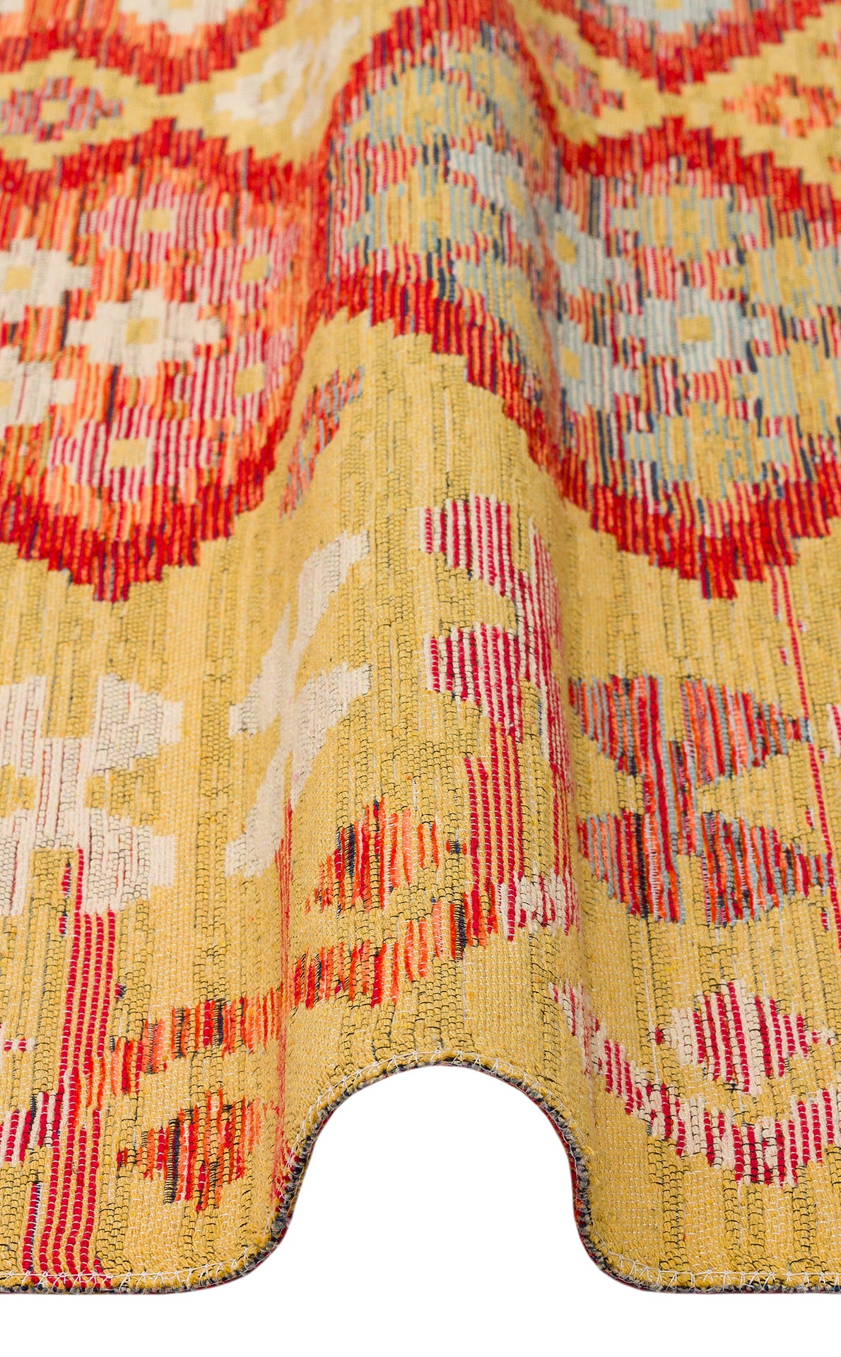 A close-up of the Crimson Dot - Kilim - NMD03 polyester flat weave rug features a yellow background with red and white geometric patterns and a wavy, folded edge.
