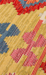 A close-up of the Crimson Dot - Kilim - NMD03 polyester flat weave rug, with yellow, blue, red, and white threads in a bold abstract geometric pattern. The texture and vibrant colors are clearly visible.