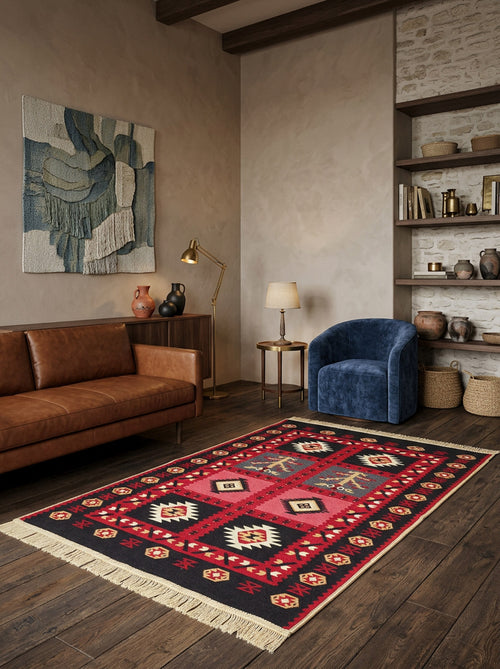 Load image 1 in gallery view. A cozy living room features a brown leather sofa, blue armchair, Crimson Form - Washable Reversible Kilims - AR28, wooden floors, lamp, shelves with books and baskets, and textured beige walls with abstract art.