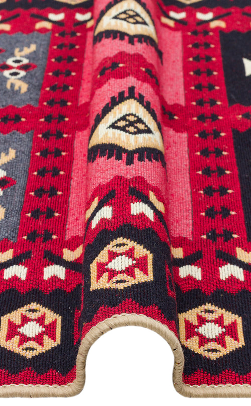 Load image 1 in gallery view. A close-up of Crimson Form - Washable Reversible Kilims - AR28, displaying vibrant tribal geometric patterns in red, black, cream, and yellow with a beige stitched border and a folded edge. This kilim rug is washable and features intricate detailing.