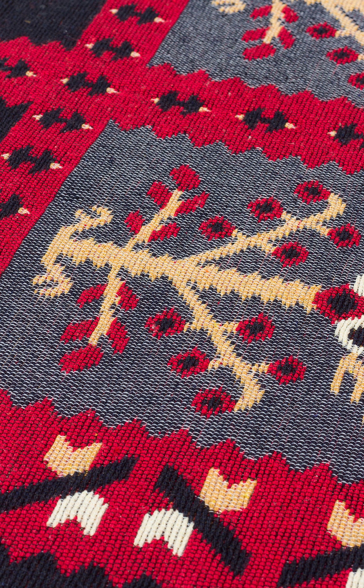 A close-up of Crimson Form - Washable Reversible Kilims - AR28 highlights bold red, blue, yellow, and white geometric patterns—zigzags, trees, and diamonds—with clearly visible textured threads on this striking reversible rug.