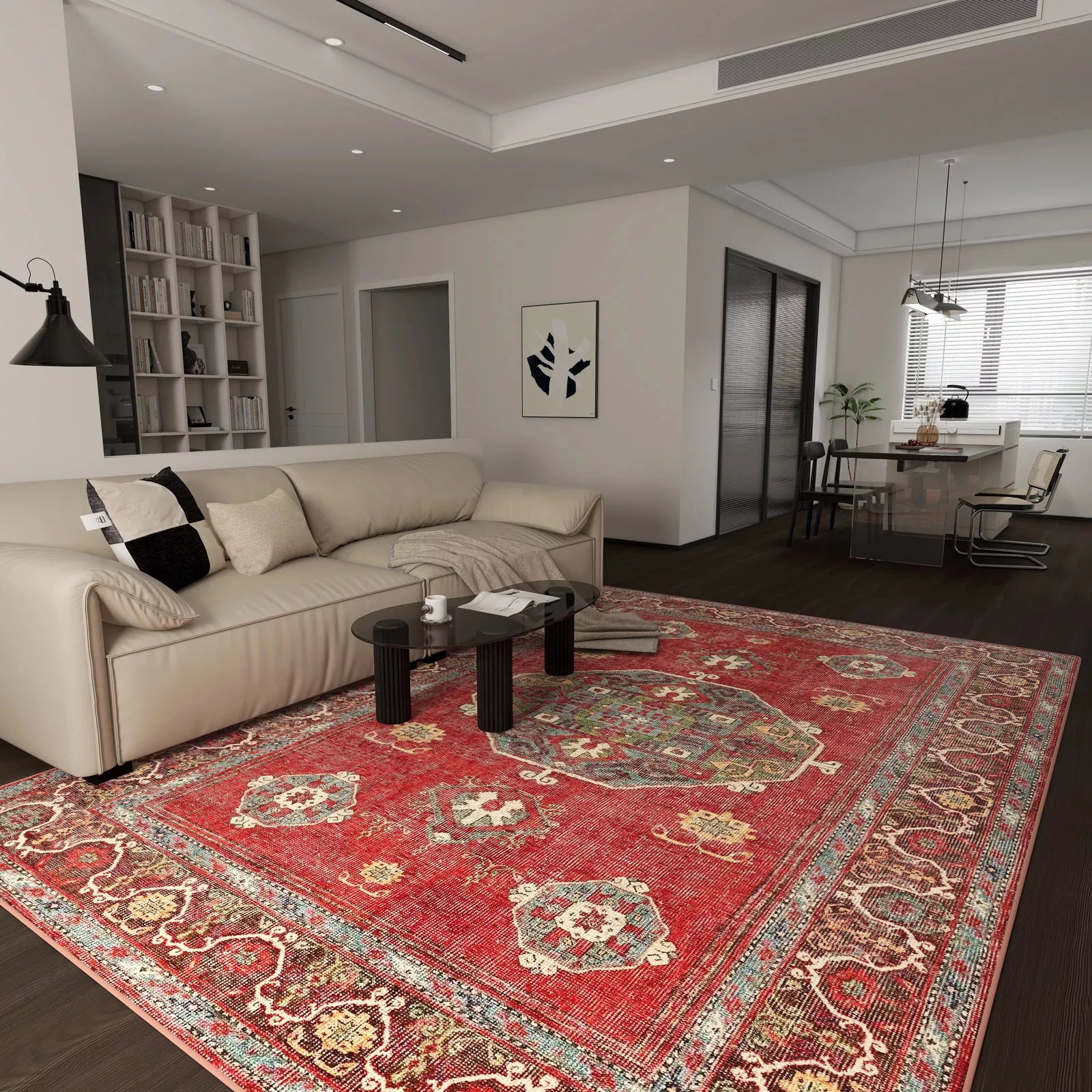 A modern living room features a beige sofa, dark round coffee tables, and the Crimson Palace - Washable Rug - JRN1041 (Custom Size) in rich red on dark wood floors. The open space connects to a dining area and kitchen with white walls and minimalist decor.