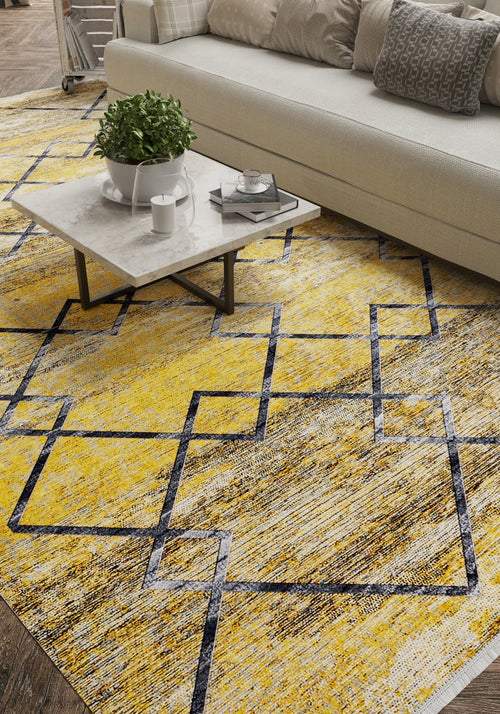 Load image 1 in gallery view. A modern living room features a light-toned sofa, gray and white cushions, a marble coffee table with accents, and the Crossed Connections - Washable Rug - JR1181 (Custom Size) in yellow-gold with a bold geometric black and white pattern.