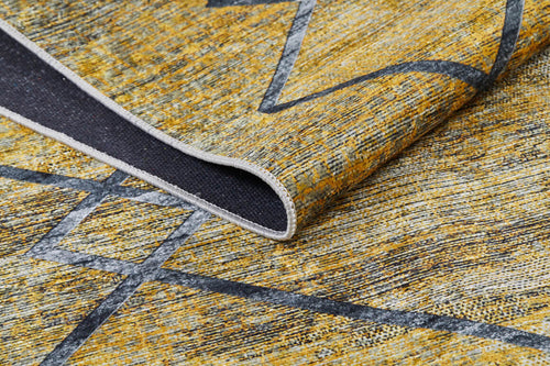 Load image 1 in gallery view. A close-up of the Crossed Connections - Washable Rug - JR1181 (Custom Size) in yellow-gold, featuring a geometric pattern and durable design for high-traffic areas, shows a corner folded to reveal its dark underside.