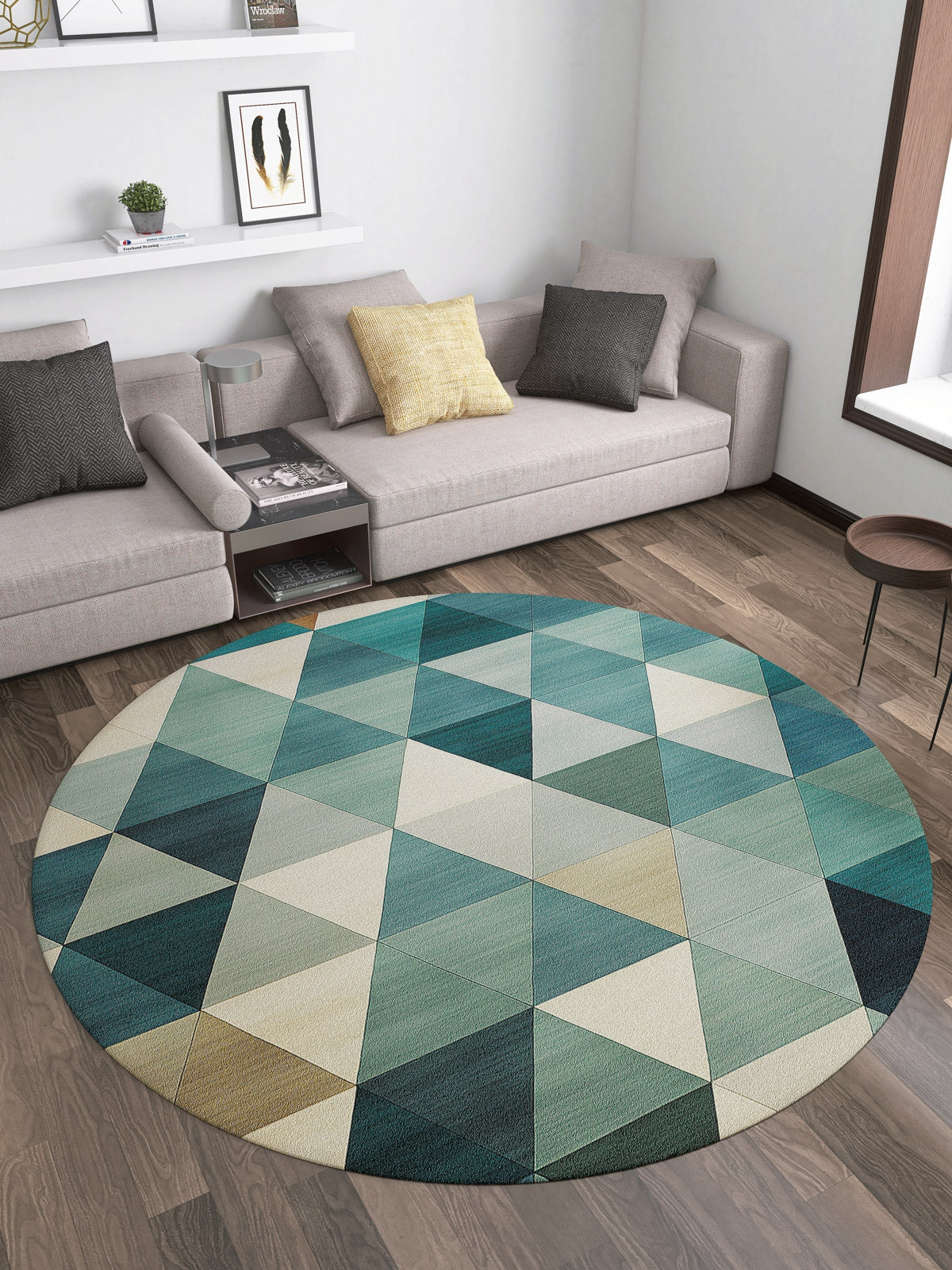 A modern living room features a gray sectional, neutral cushions, a round coffee table, white shelves with books and decor, and the Cubism Collage Blue Washable Rug - MDJ008 with geometric patterns—perfect for high-traffic wooden floors.