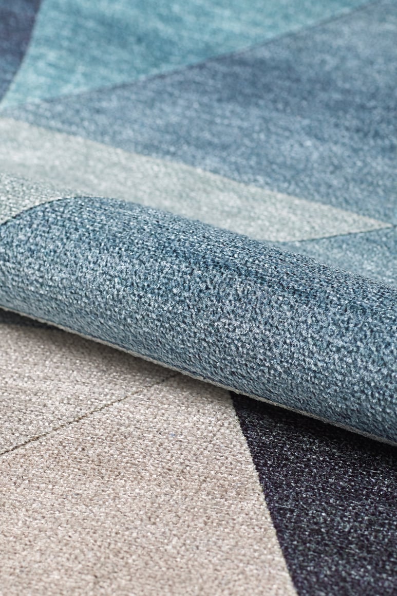 Close-up of the Cubism Collage Blue Washable Rug - MDJ008 (Custom Size), folded to showcase its geometric pattern in blue, gray, and beige tones with a textured surface—perfect for high-traffic areas.