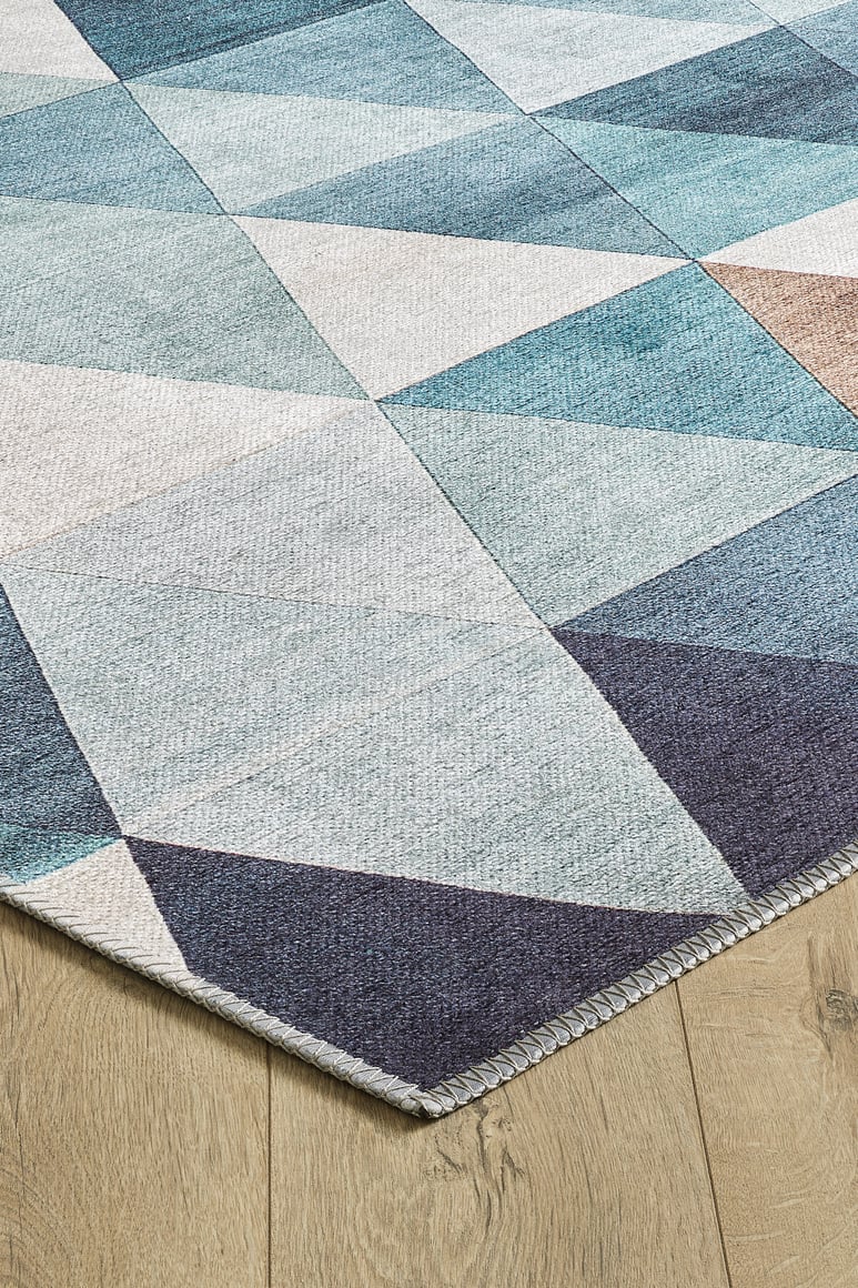 A close-up of the Cubism Collage Blue Washable Rug - MDJ008 (Custom Size), featuring blue, teal, gray, and beige geometric triangles—ideal for high-traffic areas and shown on a light wood floor.