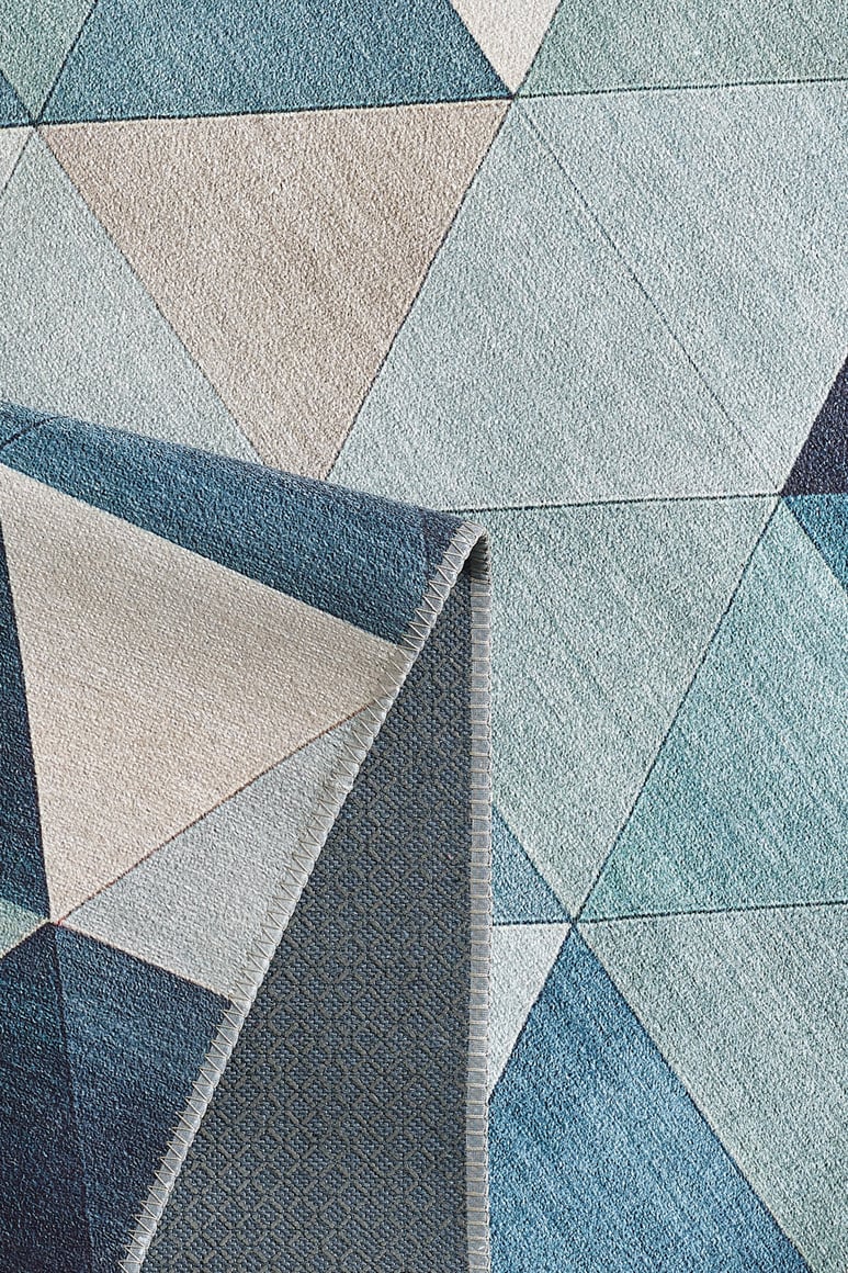 The Cubism Collage Blue Washable Rug - MDJ008 (Custom Size) features overlapping triangles and polygons in blue, gray, and beige tones with a folded corner showing the underside—perfect for high-traffic areas.