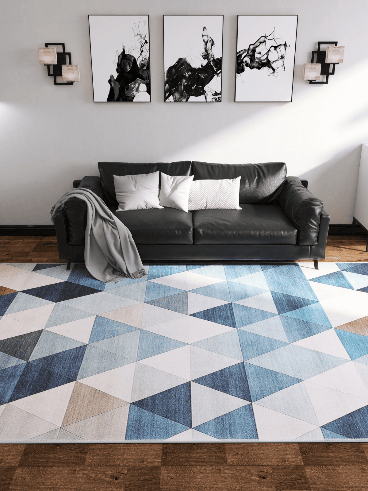 A modern living room with a black sofa, white and gray pillows, a gray throw, and the Cubism Collage Blue Washable Rug - MDJ008 (Custom Size), ideal for high-traffic areas. Three abstract artworks and two wall lights hang above the sofa on wooden flooring.
