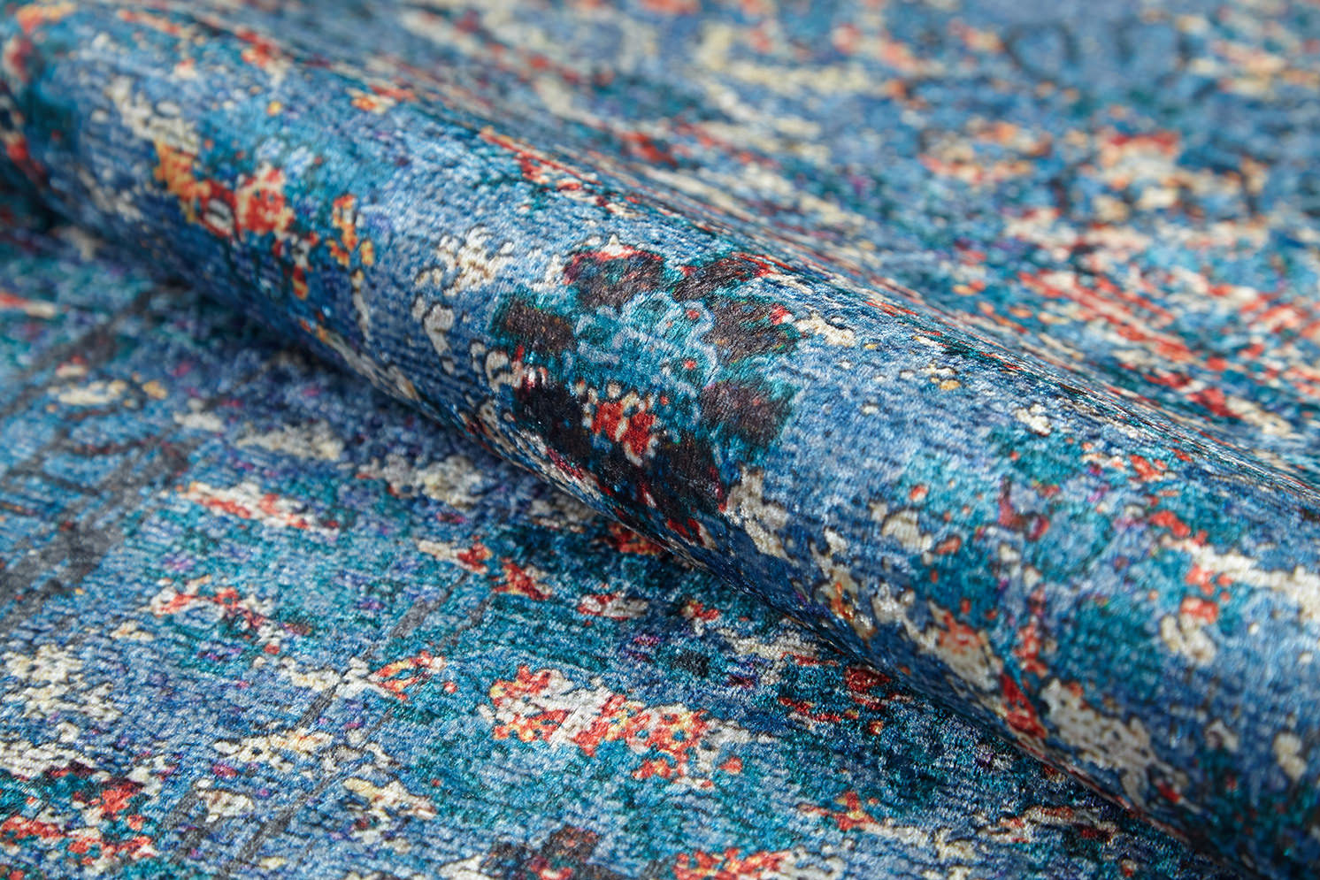 Close-up of the Desert Diamond - Washable Rug - JR5071 (Custom Size), featuring a blue base with striking patterns and multicolored specks—red, white, and black—partially rolled up; perfect for washable, high-traffic use.