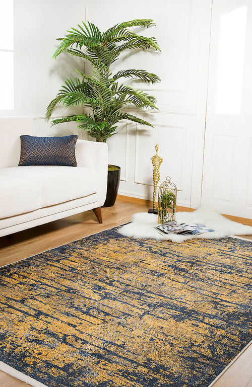 Load image 1 in gallery view. A modern living room with a white sofa, patterned cushion, large potted plant, Diagonal Dash - Washable Rug - JR1310 (Custom Size) in abstract blue and gold, white fur rug, decorative birdcage, golden statue, and magazines on a wooden floor.