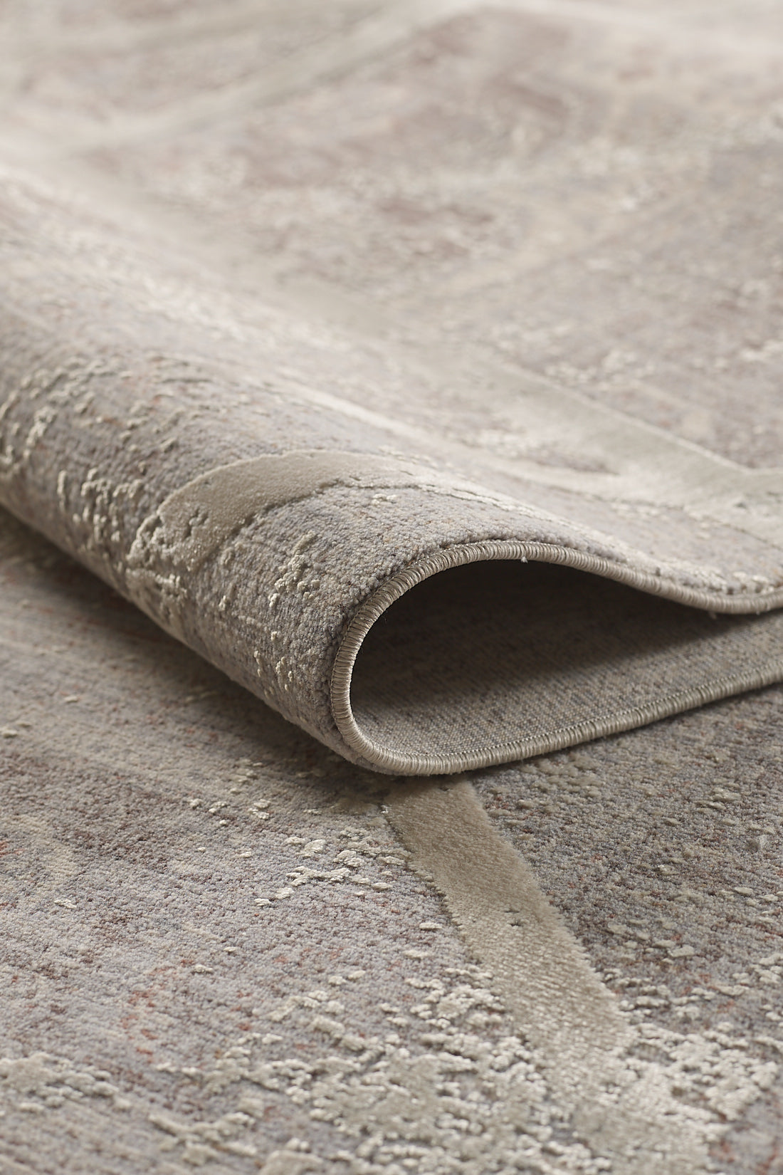 A close-up of the Dominant Lineage Modern Rug - Bright - M633M, featuring a textured, neutral-toned geometric pattern in beige and gray with one edge curled to showcase its thickness and detailed weaving.