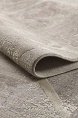 A close-up of the Dominant Lineage Modern Rug - Bright - M633M, featuring a textured, neutral-toned geometric pattern in beige and gray with one edge curled to showcase its thickness and detailed weaving.