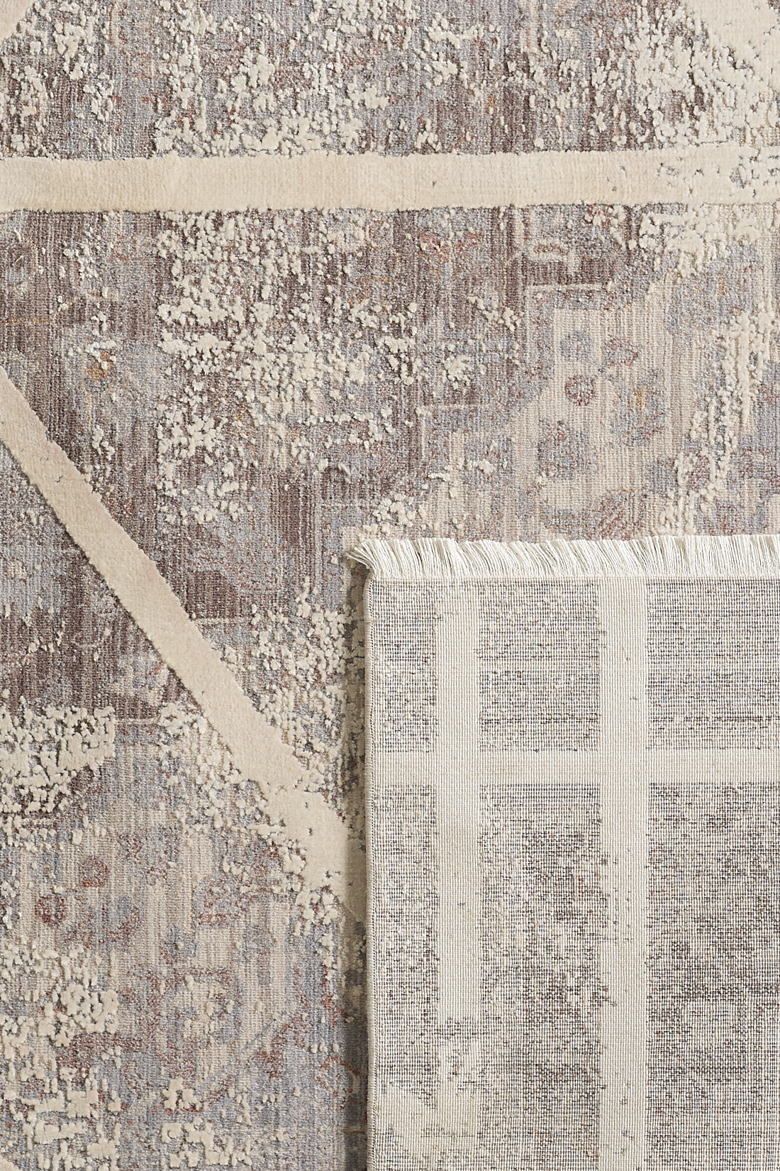A close-up of the Dominant Lineage Modern Rug - Bright - M633M, featuring abstract beige and gray patterns, with a corner flipped to display the lighter patterned underside and fringe.