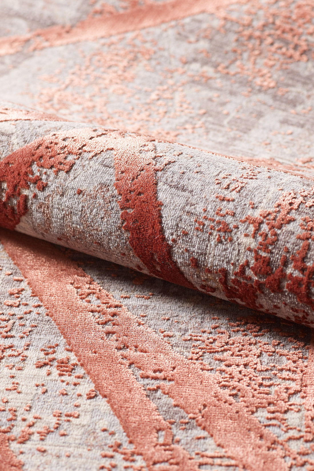A close-up of the Dominant Lineage Modern Rug - Coral (HRD003), showing its plush, machine-made texture and raised abstract rust and blush pattern on a light gray background. The fabric is slightly rolled to highlight its softness.