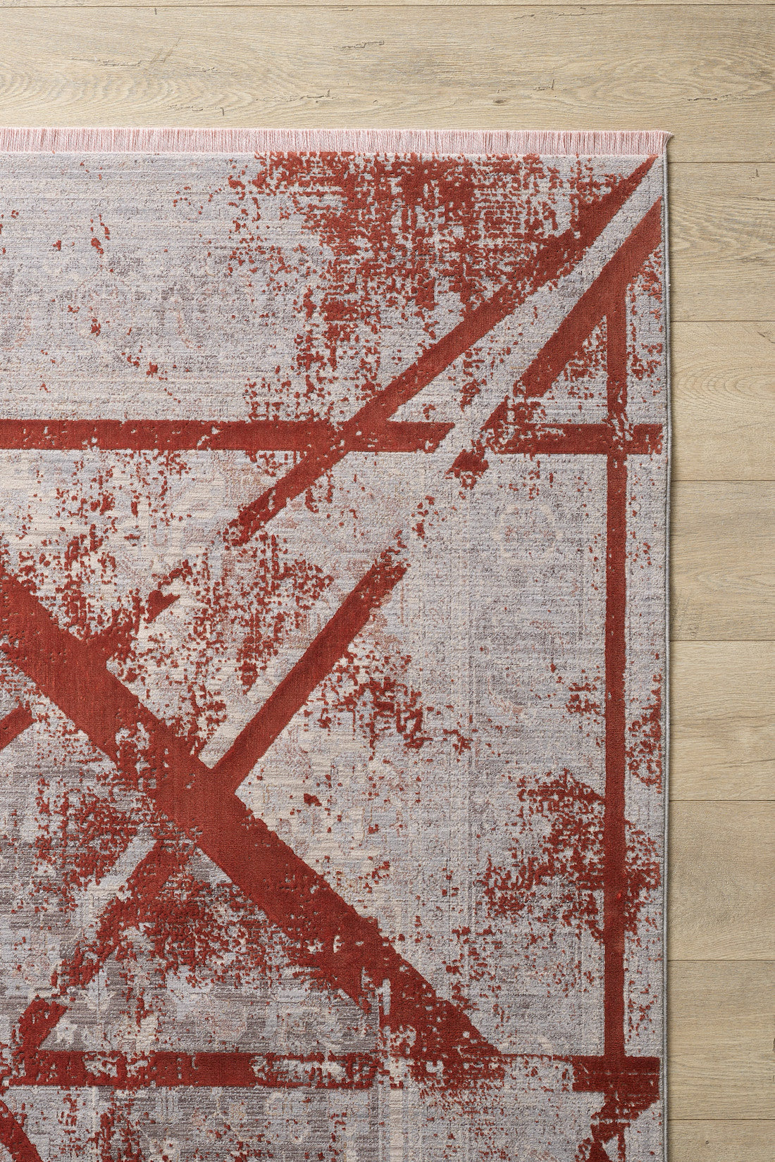 The Dominant Lineage Modern Rug - Coral (HRD003) features an abstract red geometric design on a light grey background. Displayed on a light wood floor, only one corner of the rug is visible.