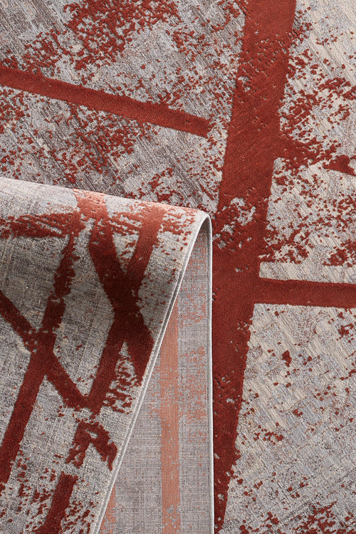 Load image 1 in gallery view. A close-up of the Dominant Lineage Modern Rug - Coral - HRD003, machine-made with a folded corner, displaying intersecting red lines and textured coral patches on a gray abstract geometric background.