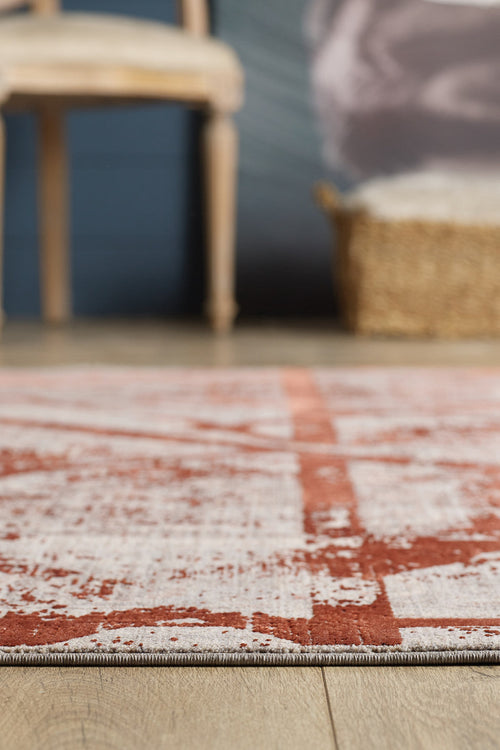 Load image 1 in gallery view. A close-up of the Dominant Lineage Modern Rug - Coral - HRD003 featuring a red and white geometric pattern on a wooden floor, with a blurred wooden chair and woven basket in the background.