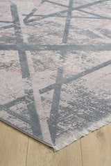 A close-up of the Dominant Lineage Modern Rug - Grey - HRD006, showcasing its geometric gray and light pink pattern with intersecting lines and a fringed edge, placed on a light wood floor.