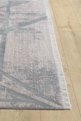 A close-up of the Dominant Lineage Modern Rug - Grey (HRD006) shows its light pink and gray abstract pattern and short white fringe, placed on a light wood floor.