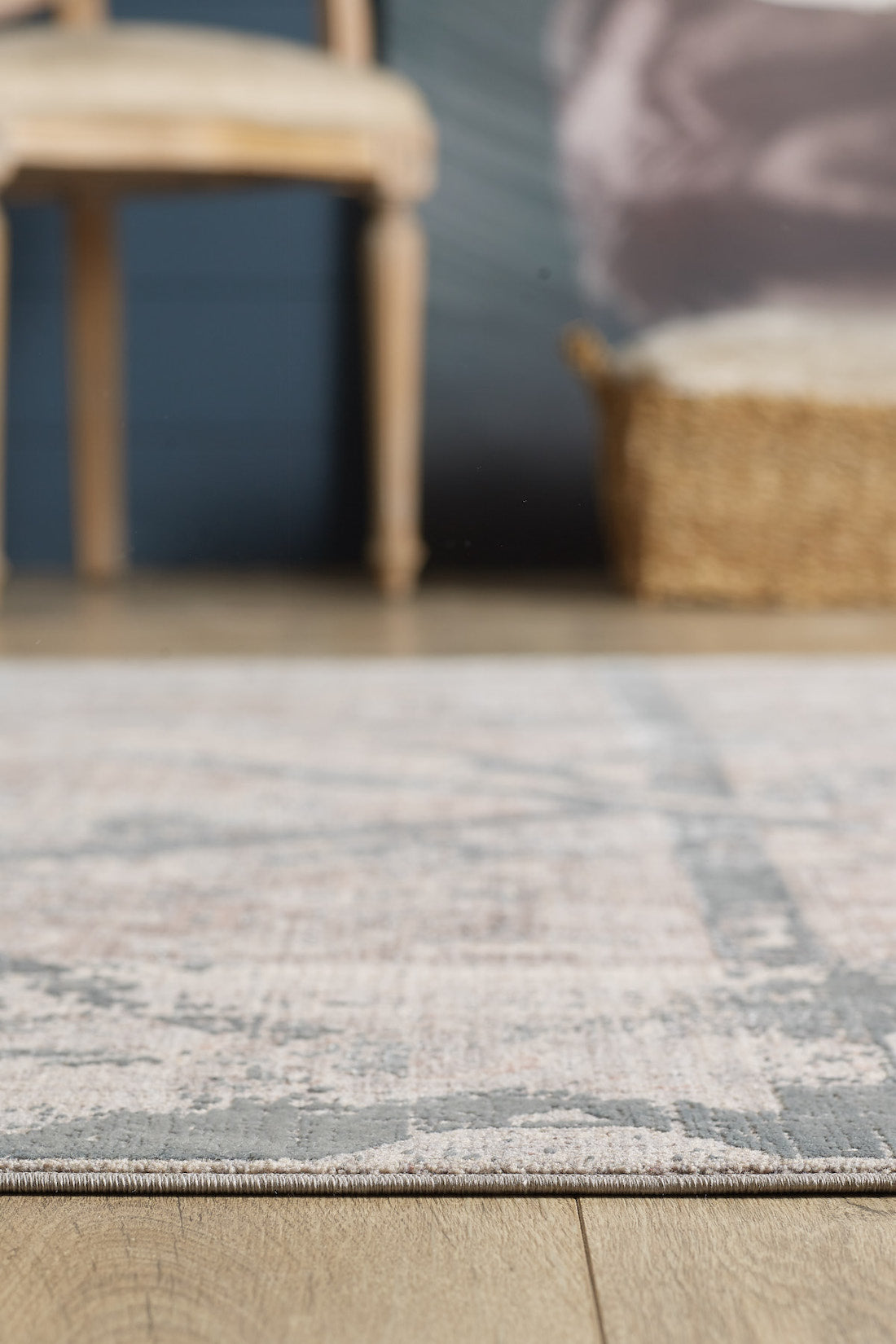 A close-up of the Dominant Lineage Modern Rug - Grey - HRD006 on a wooden floor, with a blurred wooden chair and woven basket visible in the background.