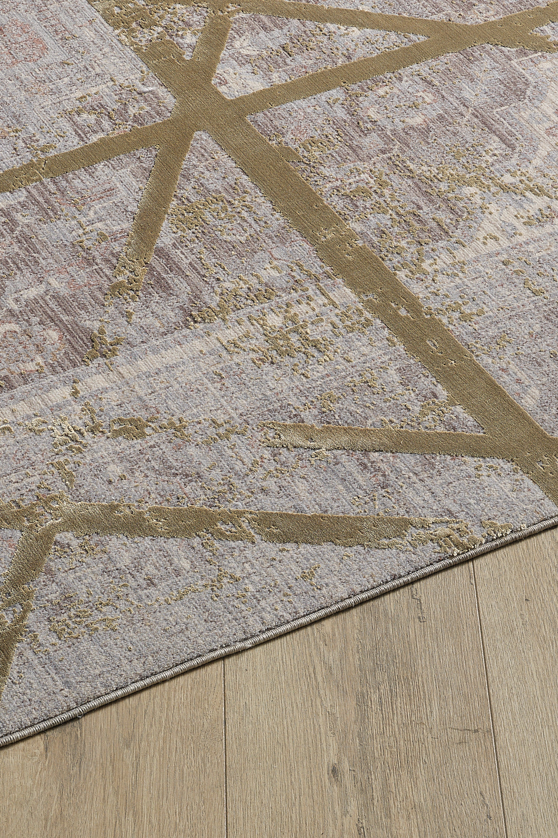 A close-up of the Dominant Lineage Modern Rug - Harvest - M633N shows intersecting gold lines on a textured, muted background, partially on a wooden floor.