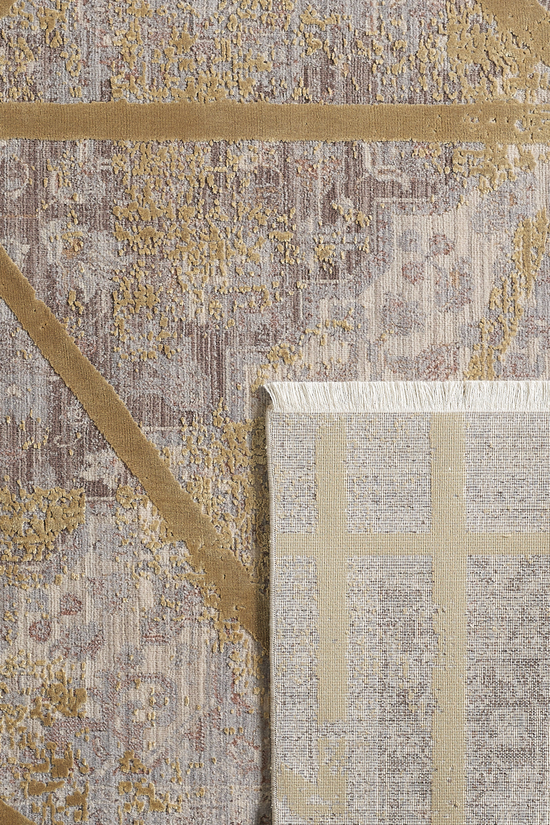 A close-up of the Dominant Lineage Modern Rug - Harvest - M633N shows its beige and gold geometric pattern; a folded corner reveals the lighter, fringed underside and reverse design, emphasizing this machine-made rug's craftsmanship.