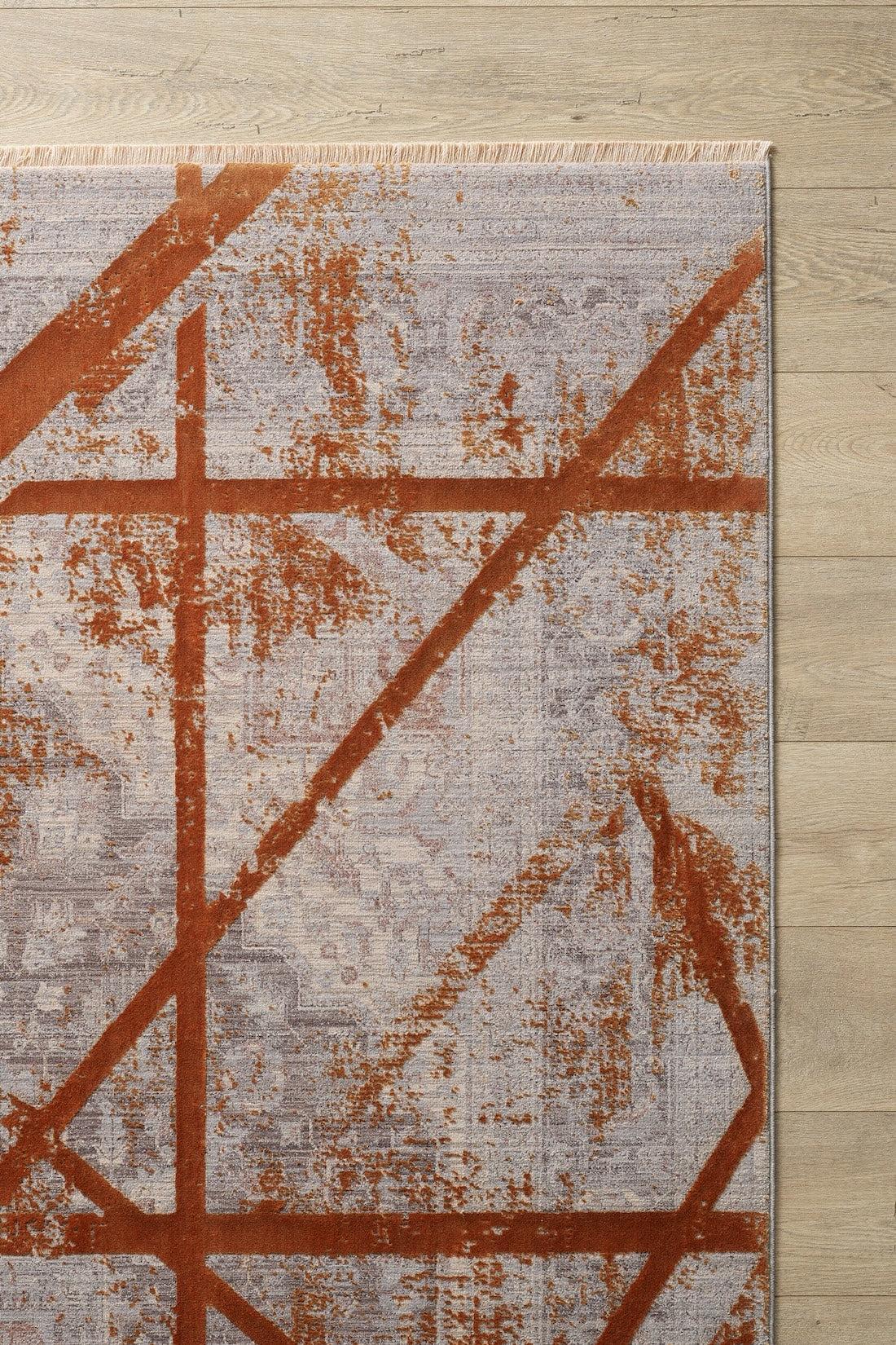 A close-up of the Dominant Lineage Modern Rug - Tangerine (HRD007) on a light wooden floor, showcasing its gray base with bold tangerine abstract lines and shapes, plus fringe detailing along one edge.