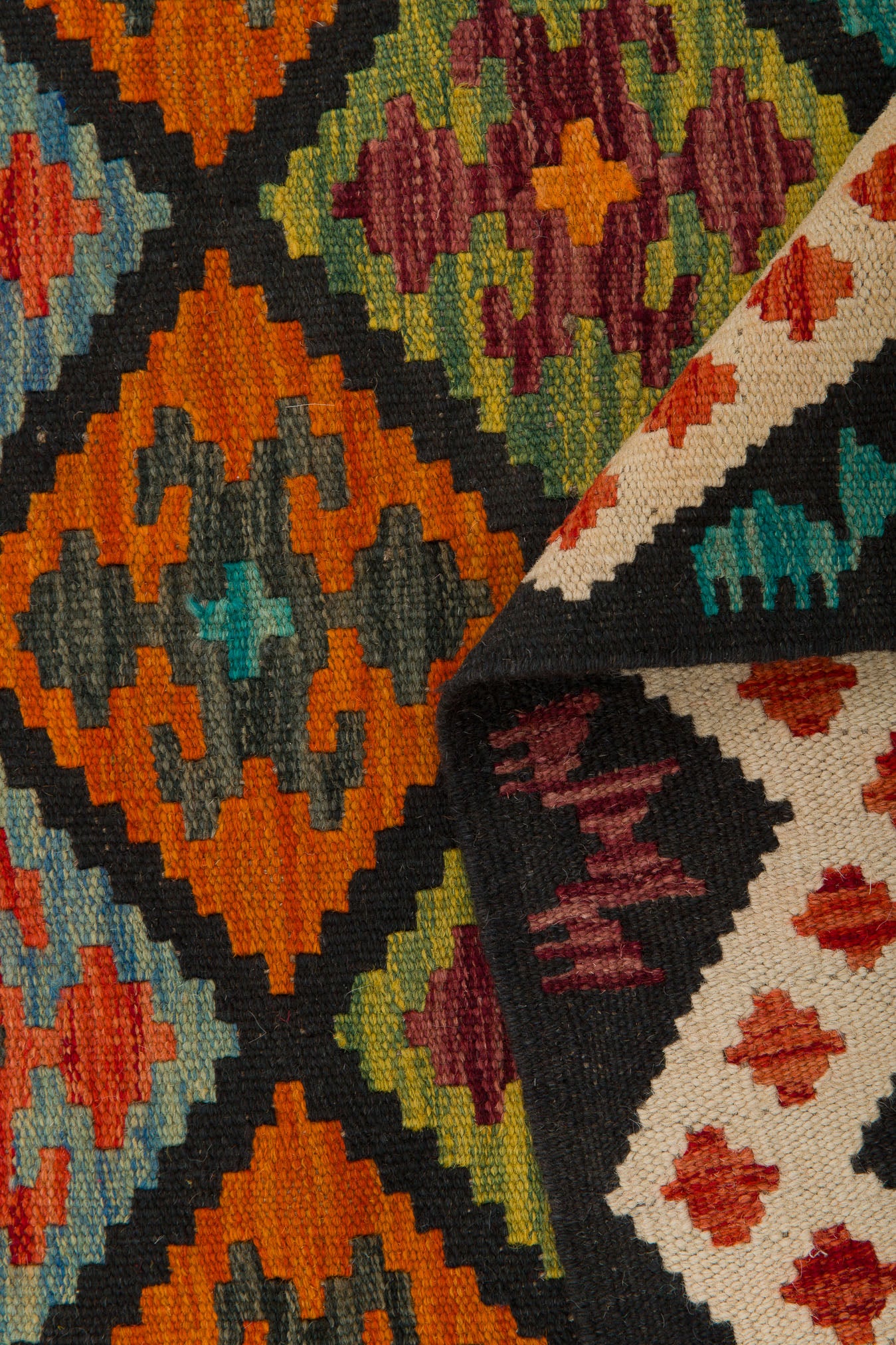 The Earthly Lines - Handwoven Kilim features vibrant geometric patterns in orange, green, blue, red, and purple. A folded corner reveals a cream underside with classic diamond and zigzag designs—hallmarks of authentic kilims.