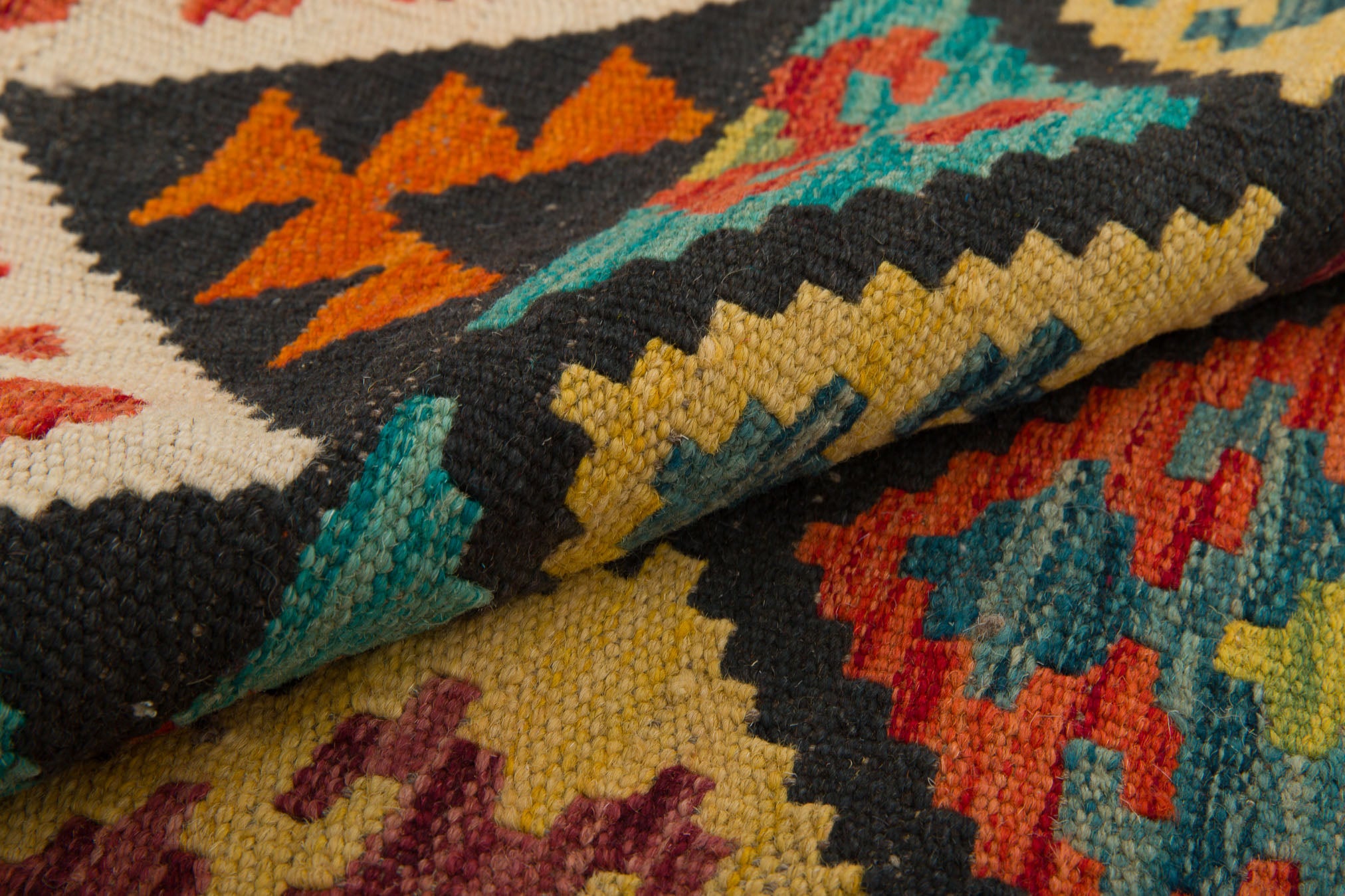 A close-up of Earthly Lines - Handwoven Kilim showcases its intricate geometric patterns in vibrant orange, teal, yellow, red, and black, with the fabric gently folded to highlight its detailed texture.