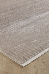 A close-up of the Earthy Textures Neutral Rug - M497J shows its beige flat pile with subtle horizontal lines and a slight sheen, placed on a light wood floor. One minimalist edge is finished with a short fringe.