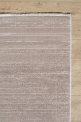 A close-up of the Earthy Textures Neutral Rug - M497J shows its rectangular, light brown minimalist design with subtle horizontal lines and a fringed top edge, placed on a light wooden floor.