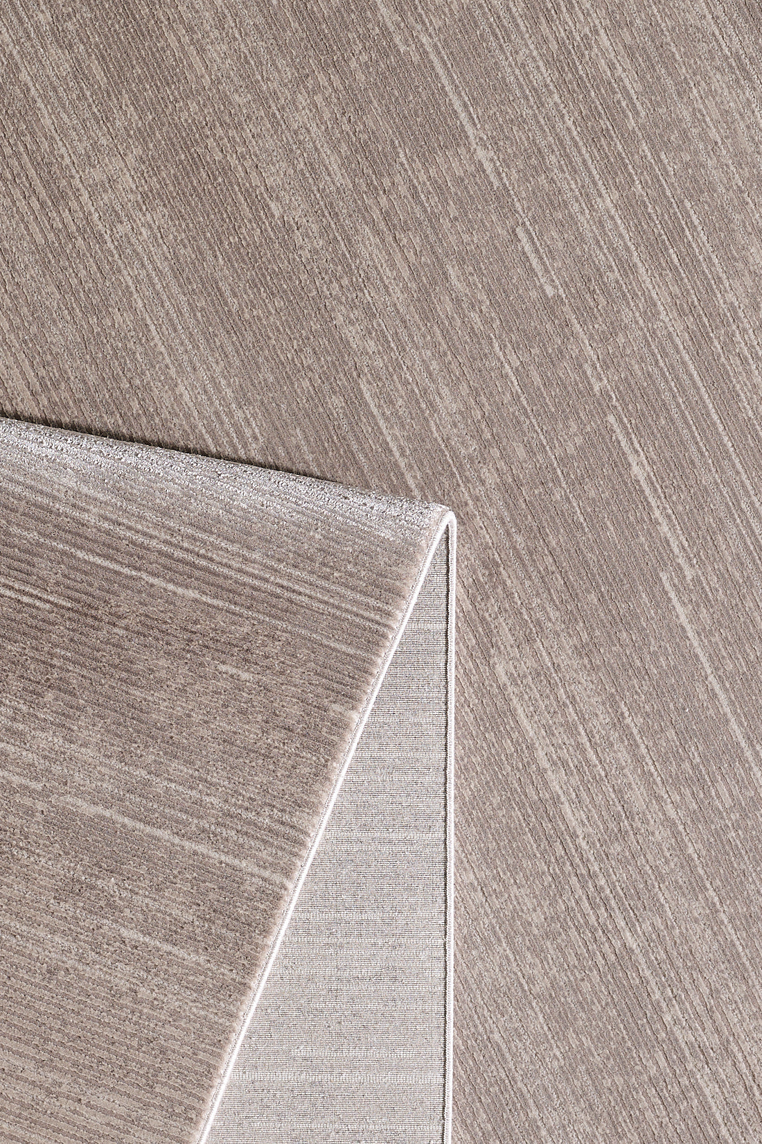 A close-up of the Earthy Textures Neutral Rug - M497J in beige, featuring a subtle linear pattern and one corner folded to display the fabric texture on both sides.