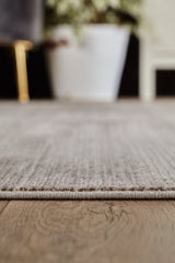 Close-up of the Earthy Textures Neutral Rug - M497J on a wooden floor, featuring its minimalist edge and a large white plant pot in the softly blurred background.