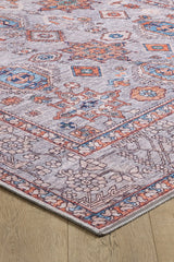 A close-up of the Echelon Bordered Washable Rug - LCC3018, featuring an intricate geometric and floral pattern in blue, orange, and cream on a light wood floor—ideal for high-traffic areas.