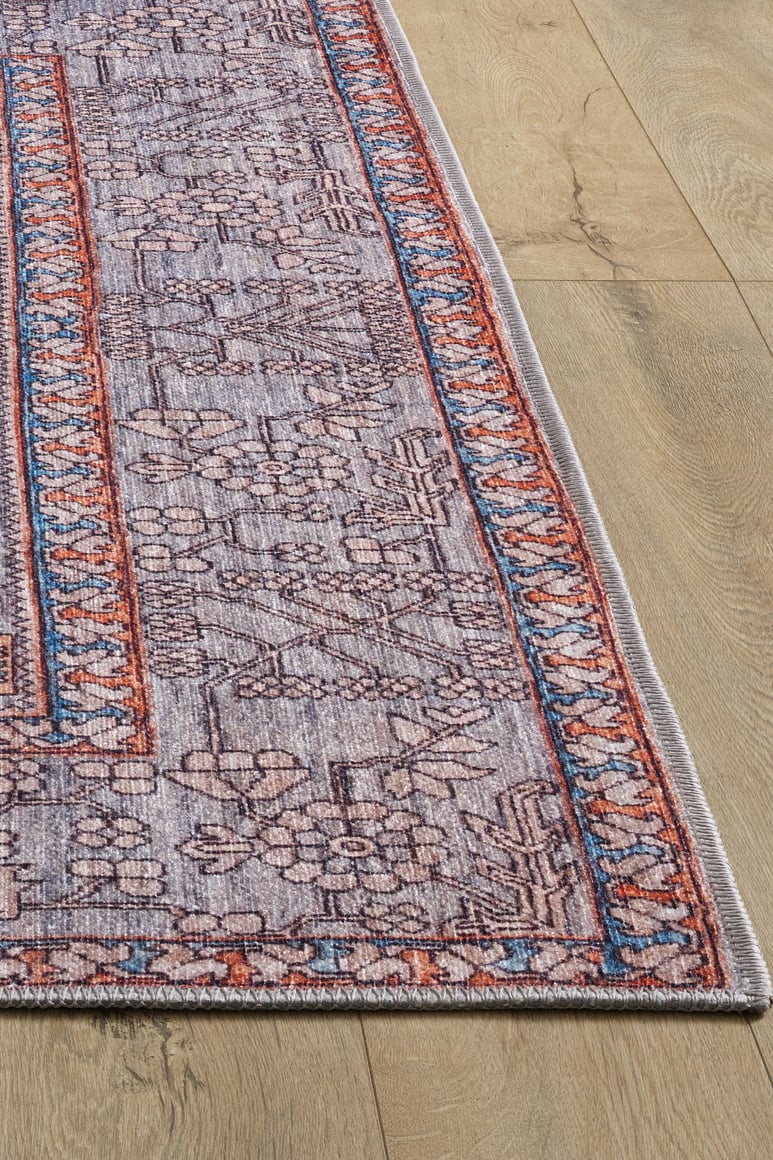 The Echelon Bordered Washable Rug - LCC3018 features a faded purple and red geometric floral pattern with blue and orange borders—perfect for high-traffic spaces and striking on light wood floors.