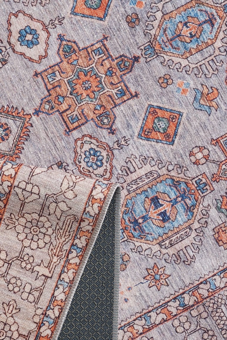 A close-up of the Echelon Bordered Washable Rug - LCC3018, featuring geometric and floral patterns in blue, rust, and beige. A folded corner displays its durable underside, making it ideal for high-traffic areas.