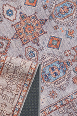 A close-up of the Echelon Bordered Washable Rug - LCC3018, featuring geometric and floral patterns in blue, rust, and beige. A folded corner displays its durable underside, making it ideal for high-traffic areas.