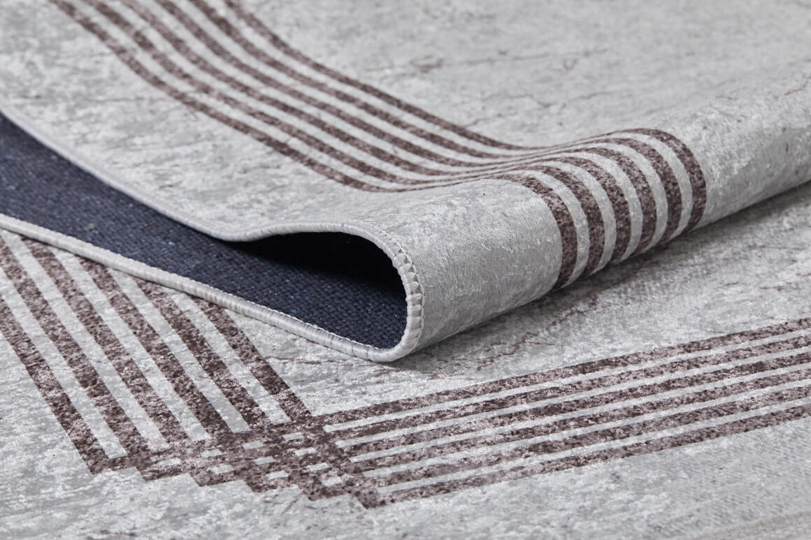A close-up of the Elegant and Chic - Washable Rug - JR1509 (Custom Size) in gray, featuring dark brown edge stripes; one corner is lifted to show the sturdy underside and stitching, making it ideal for high-traffic areas.
