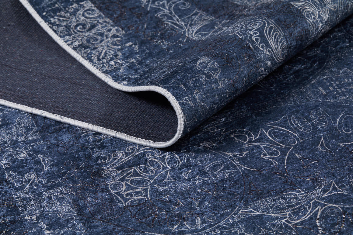 A close-up of the Elegant and Modern - Washable Rug - JR1297 (Custom Size) in blue with white abstract designs and a stitched edge, partially folded to reveal its textured dark underside—ideal for high-traffic areas.