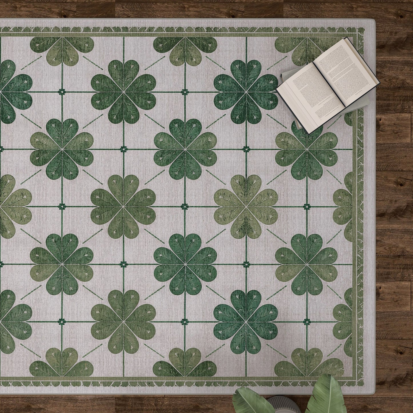 The Emerald Charm - Washable Rug - JRS013, featuring green four-leaf clovers and a subtle floral pattern, lies on a wooden floor with books and plant leaves nearby—ideal for high-traffic areas.