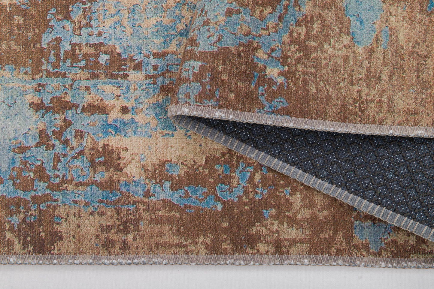 A close-up of the Enchanted Threads - Washable Rug - JRS002 (Custom Size) shows its brown, beige, and blue abstract pattern. A folded corner reveals dark, non-slip backing—washable and perfect for allergy-sensitive households.