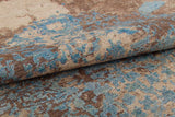 Close-up of the Enchanted Threads - Washable Rug - JRS002 (Custom Size), featuring a folded, textured surface with an abstract blue and brown pattern on beige. Its vintage, weathered look is perfect for allergy-sensitive homes and high-traffic areas.